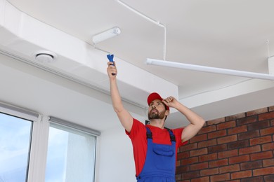 Handyman painting ceiling with roller in room
