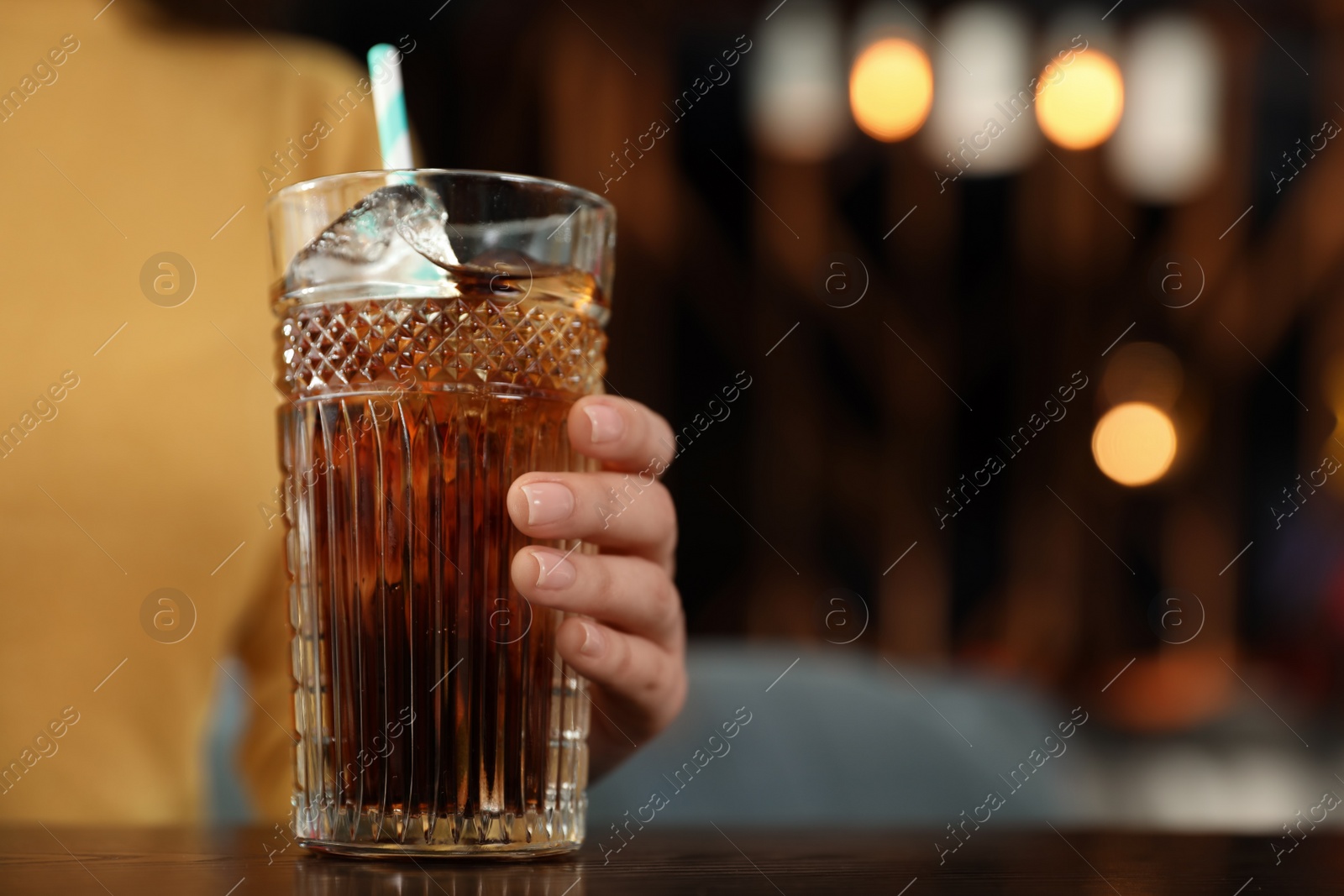 Photo of Woman with glass of refreshing cola at table indoors, closeup. Space for text