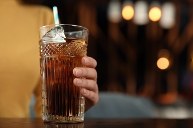 Woman with glass of refreshing cola at table indoors, closeup. Space for text