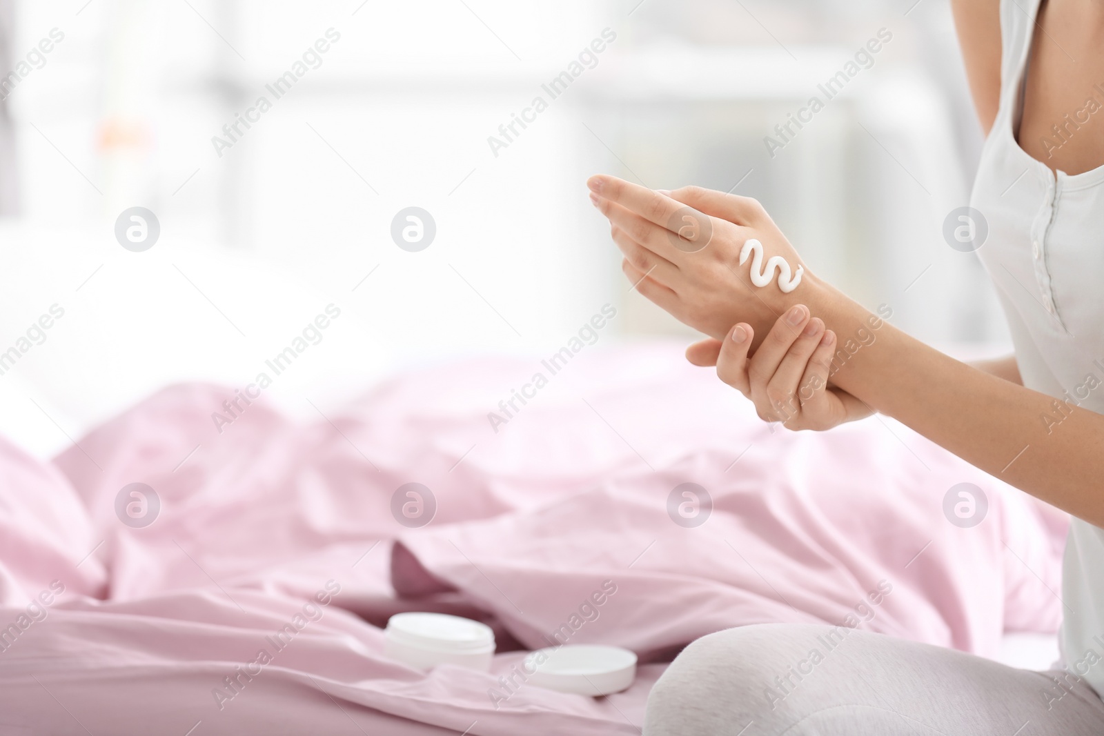 Photo of Young woman applying hand cream on bed at home