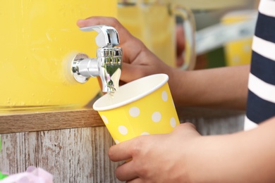 Photo of Little girl pouring natural lemonade into cup, closeup. Summer refreshing drink