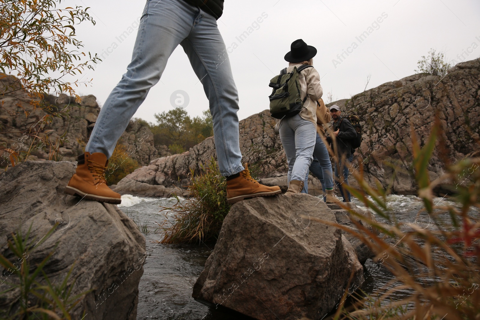 Photo of Group of friends with backpacks crossing mountain river on autumn day, closeup