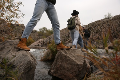 Photo of Group of friends with backpacks crossing mountain river on autumn day, closeup