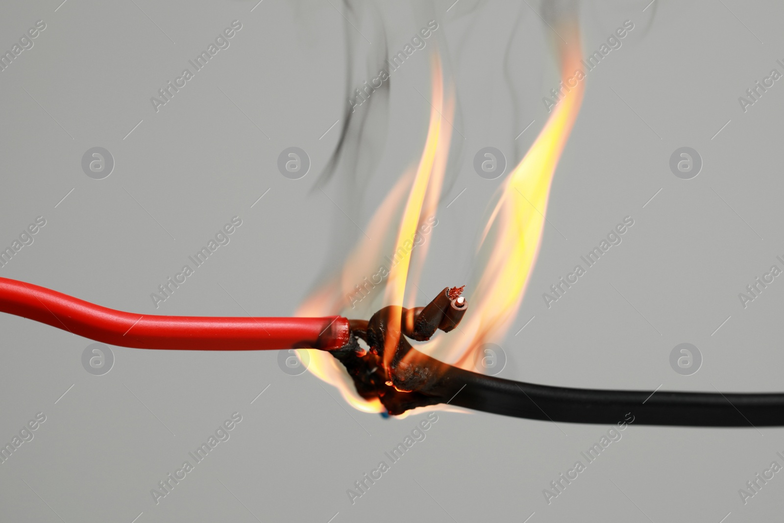 Photo of Inflamed red wire on grey background, closeup. Electrical short circuit