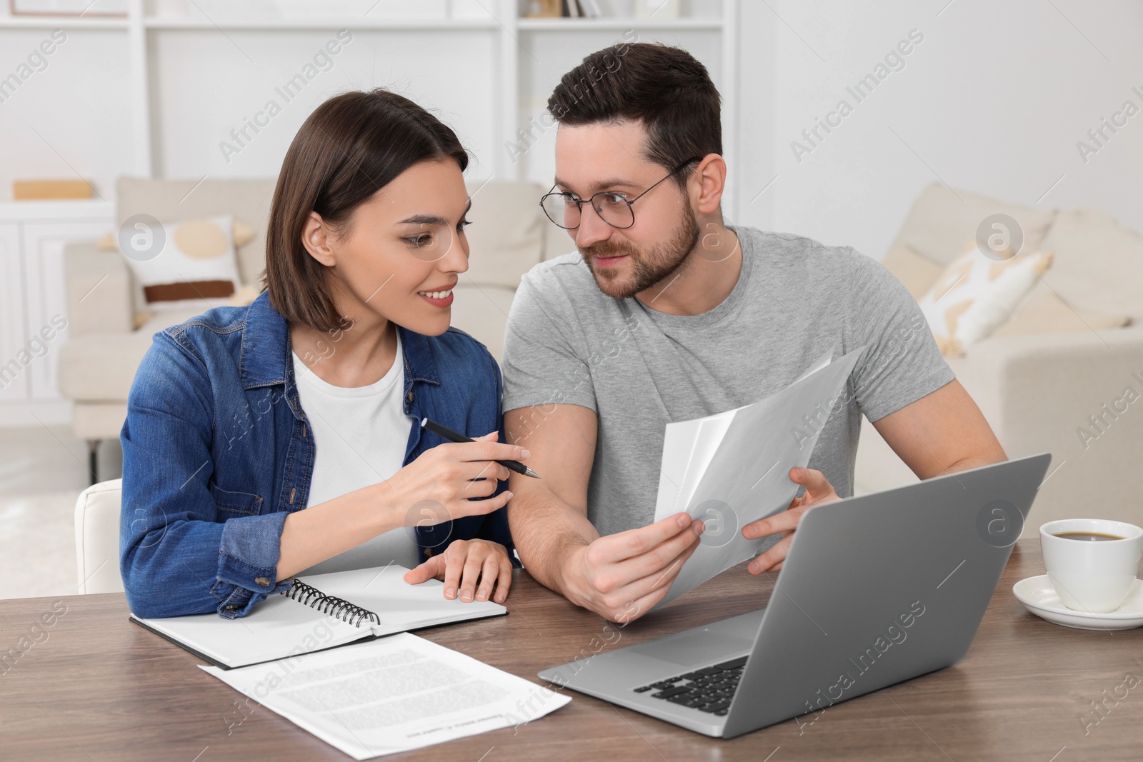 Photo of Young couple with papers discussing pension plan at wooden table indoors