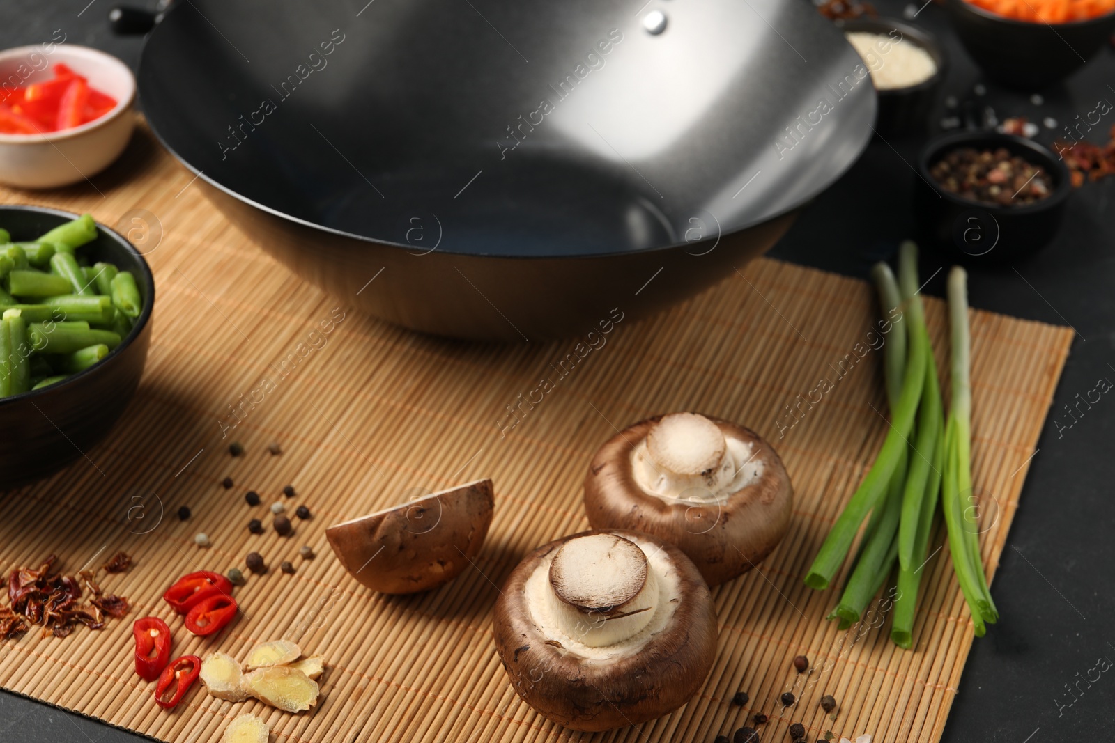 Photo of Black wok, spices and products on dark table, closeup