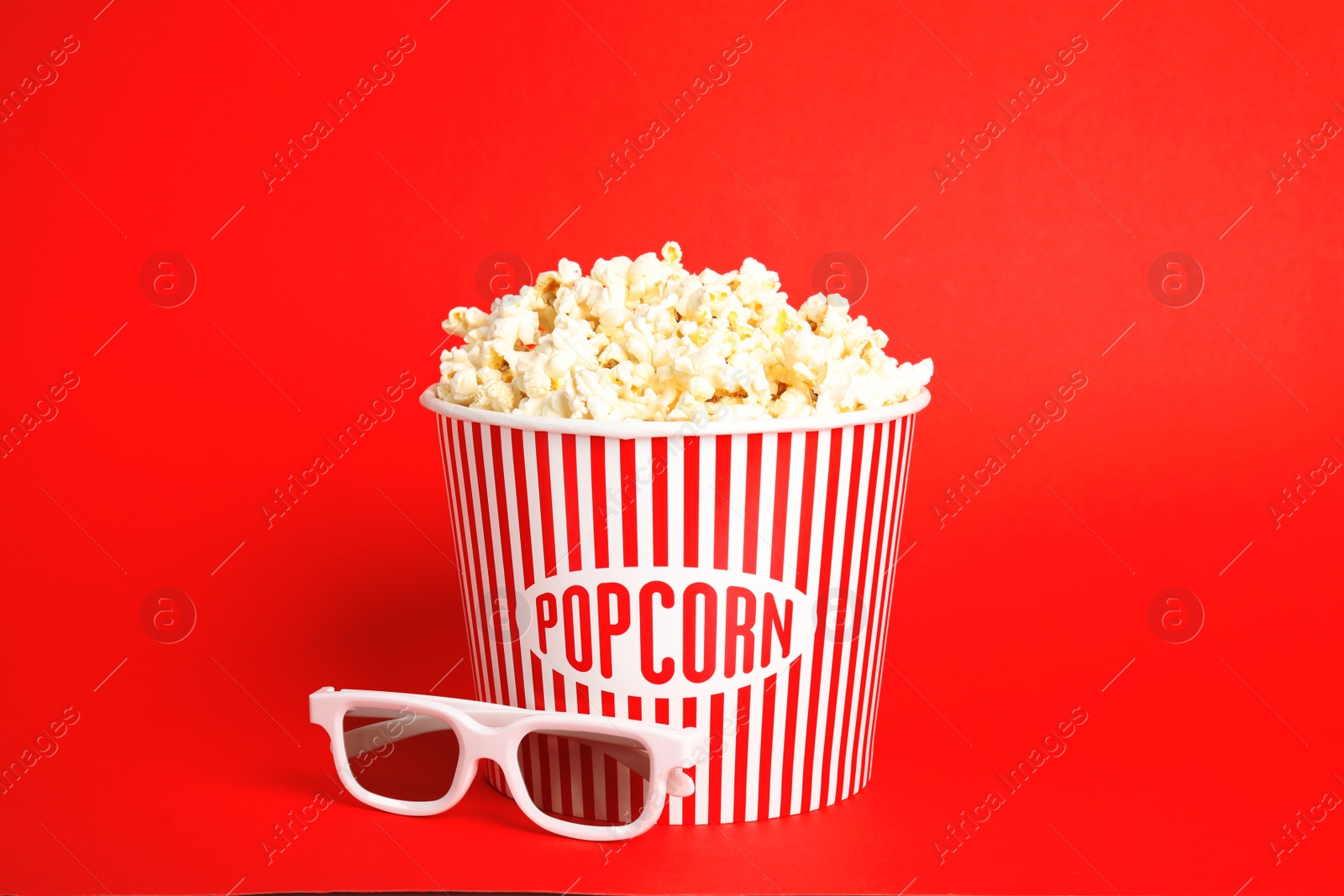 Photo of Bucket of fresh tasty popcorn and glasses on color background. Cinema snack