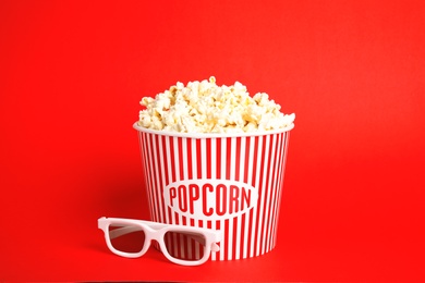 Photo of Bucket of fresh tasty popcorn and glasses on color background. Cinema snack