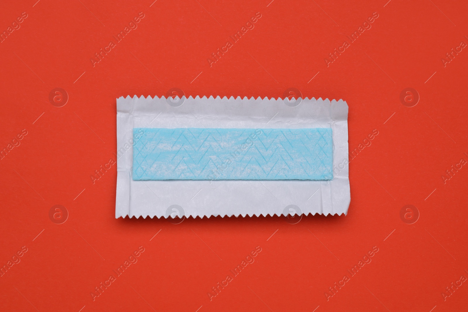 Photo of Unwrapped stick of tasty chewing gum on red background, top view