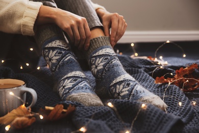 Photo of Woman wearing knitted socks on warm plaid indoors, closeup. Cozy season