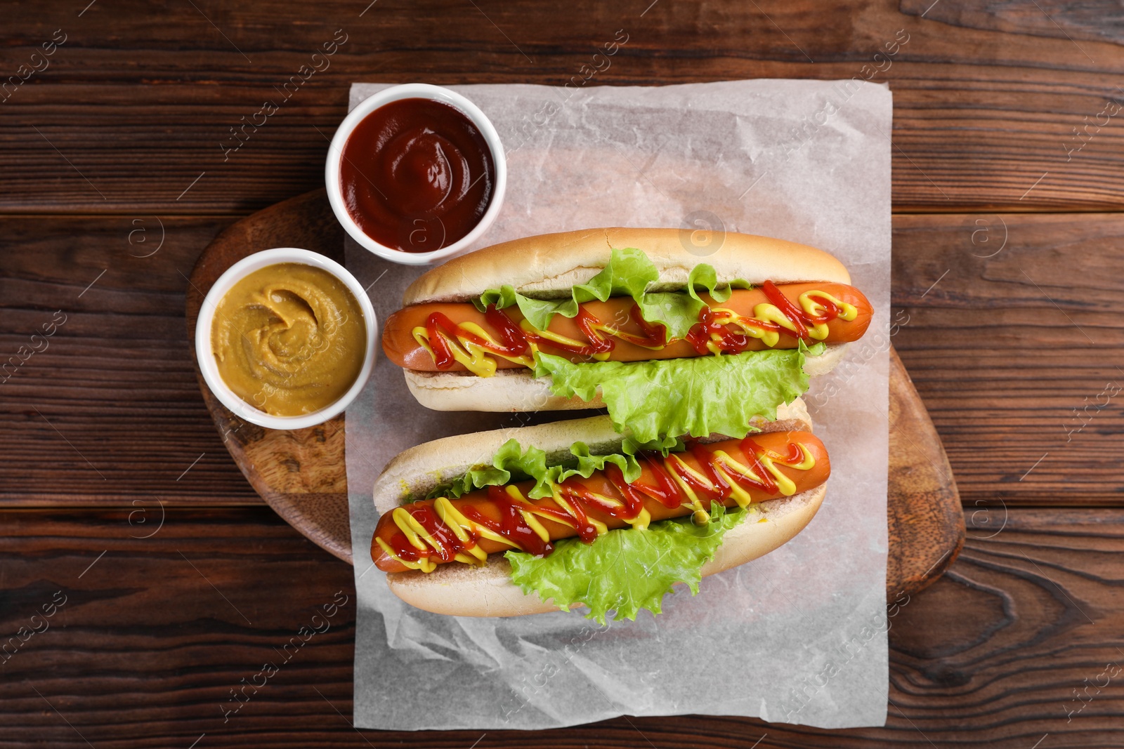 Photo of Tasty hot dogs with lettuce, ketchup and mustard on wooden table, top view