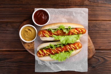 Photo of Tasty hot dogs with lettuce, ketchup and mustard on wooden table, top view