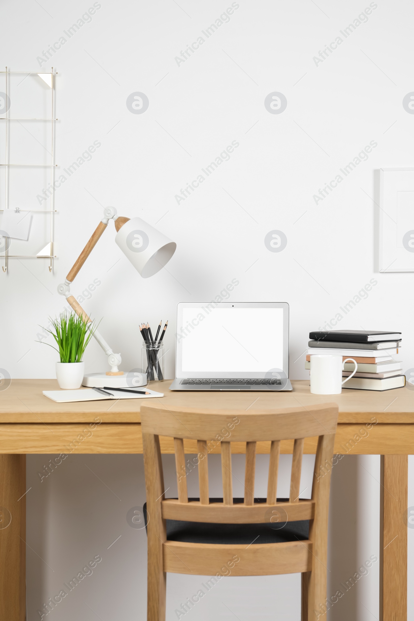 Photo of Cozy workspace with laptop, lamp and stationery on wooden desk at home