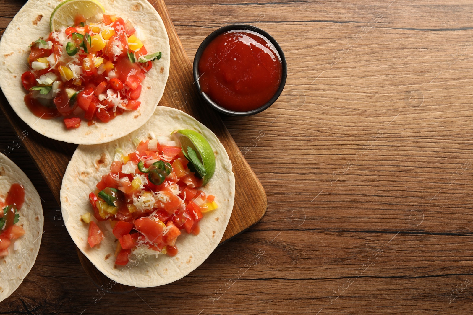 Photo of Delicious tacos with vegetables, lime and ketchup on wooden table, flat lay. Space for text