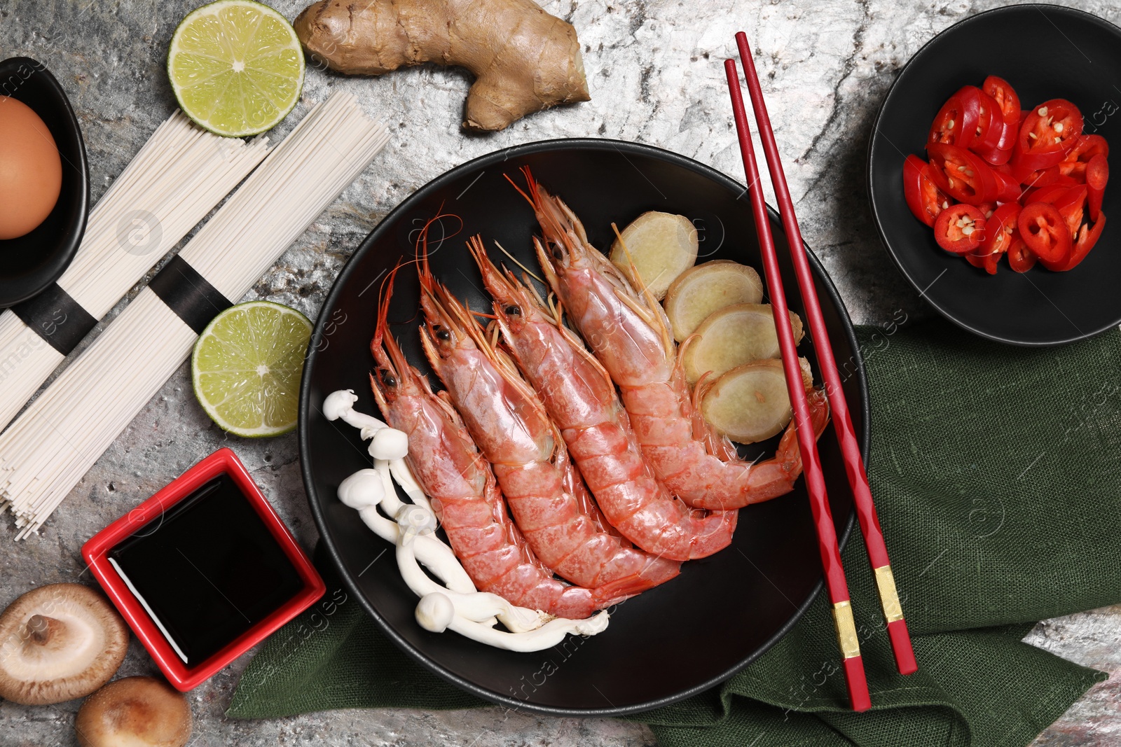 Photo of Cooking delicious ramen soup. Different ingredients and chopsticks on gray textured table, flat lay