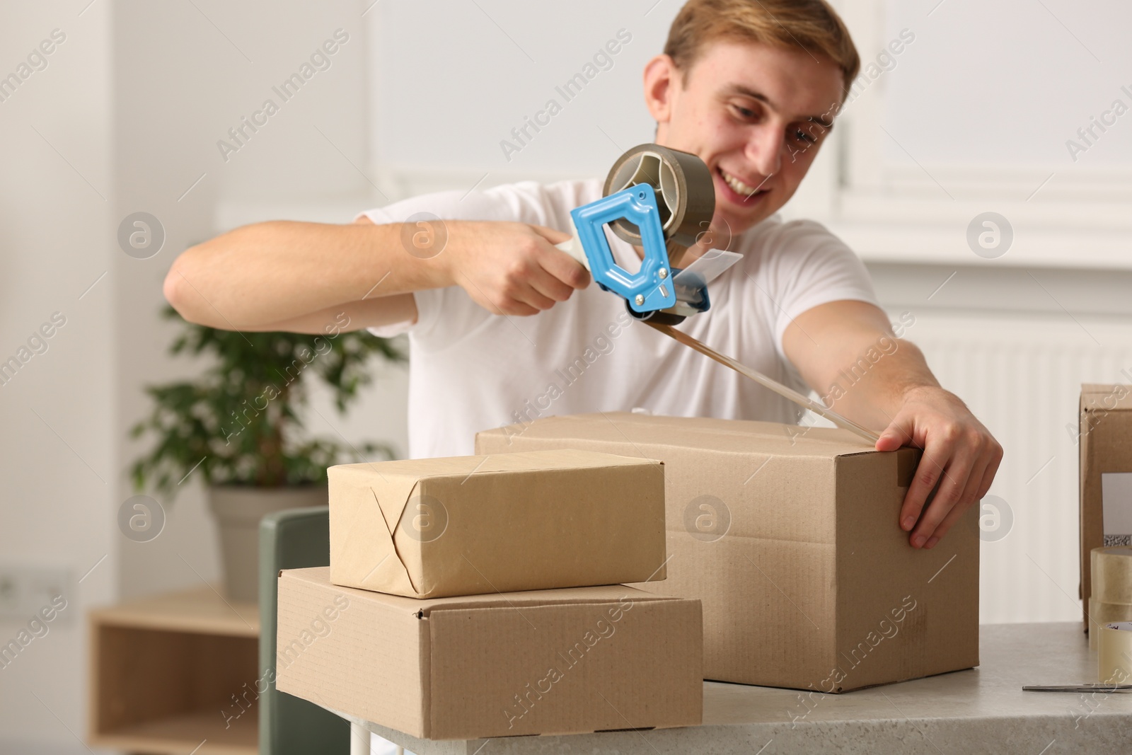 Photo of Young man packing box with adhesive tape indoors