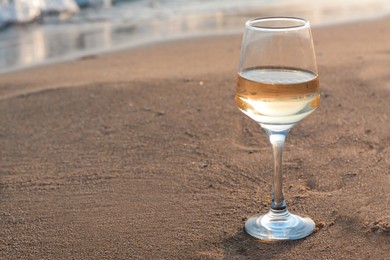 Photo of Glasstasty wine on sand near sea, space for text