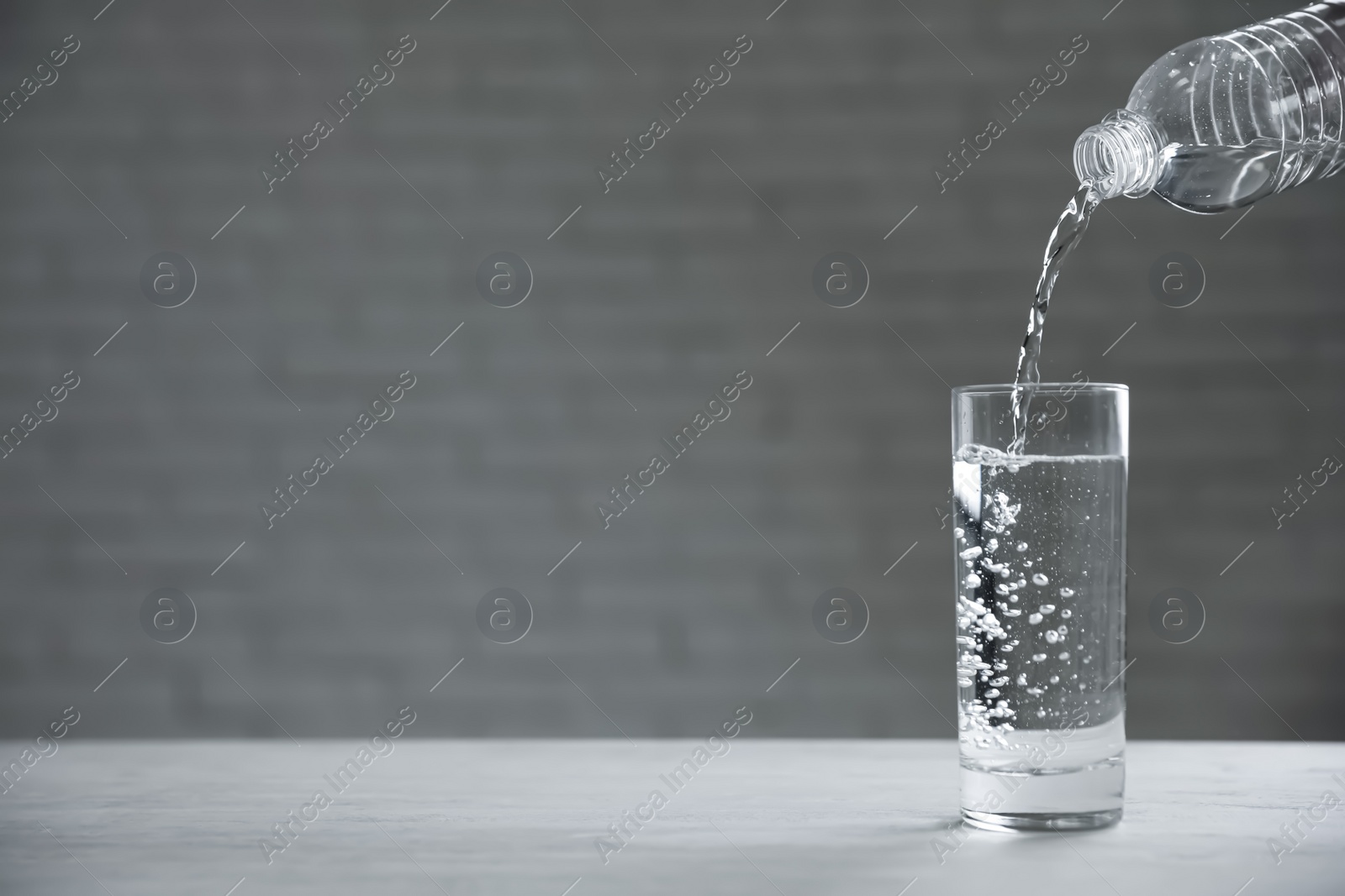 Photo of Pouring water from bottle into glass on table against blurred background. Space for text