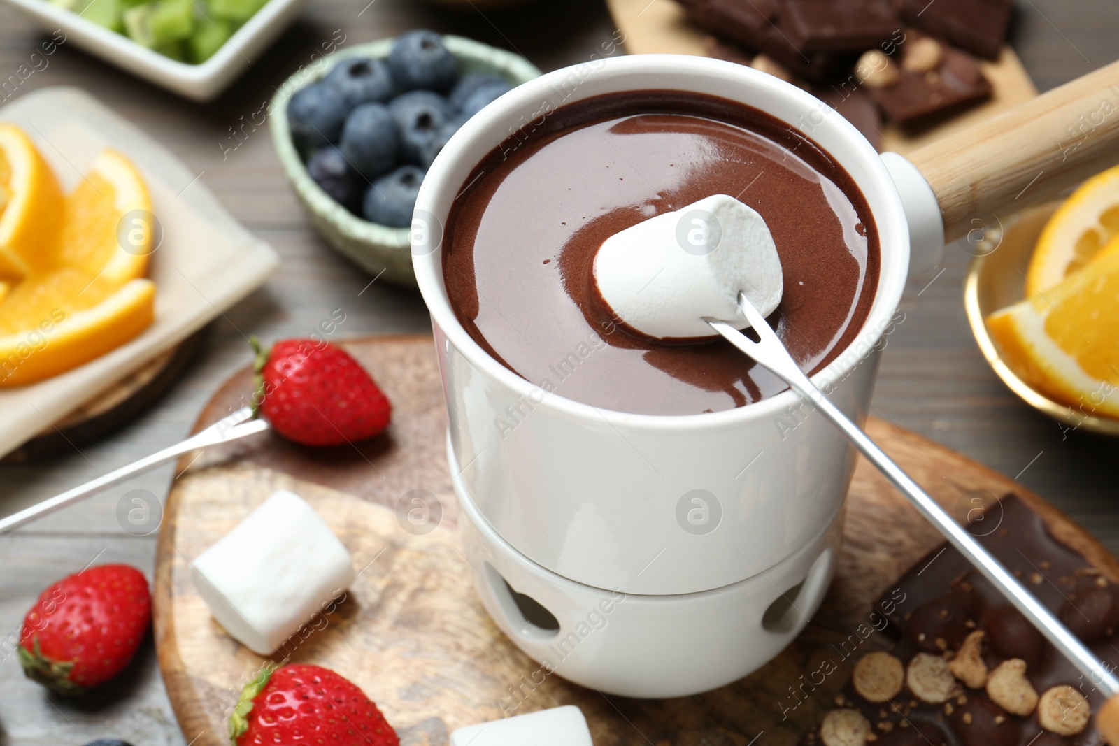 Photo of Dipping sweet marshmallow in fondue pot with melted chocolate at wooden table