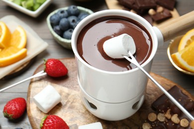 Photo of Dipping sweet marshmallow in fondue pot with melted chocolate at wooden table