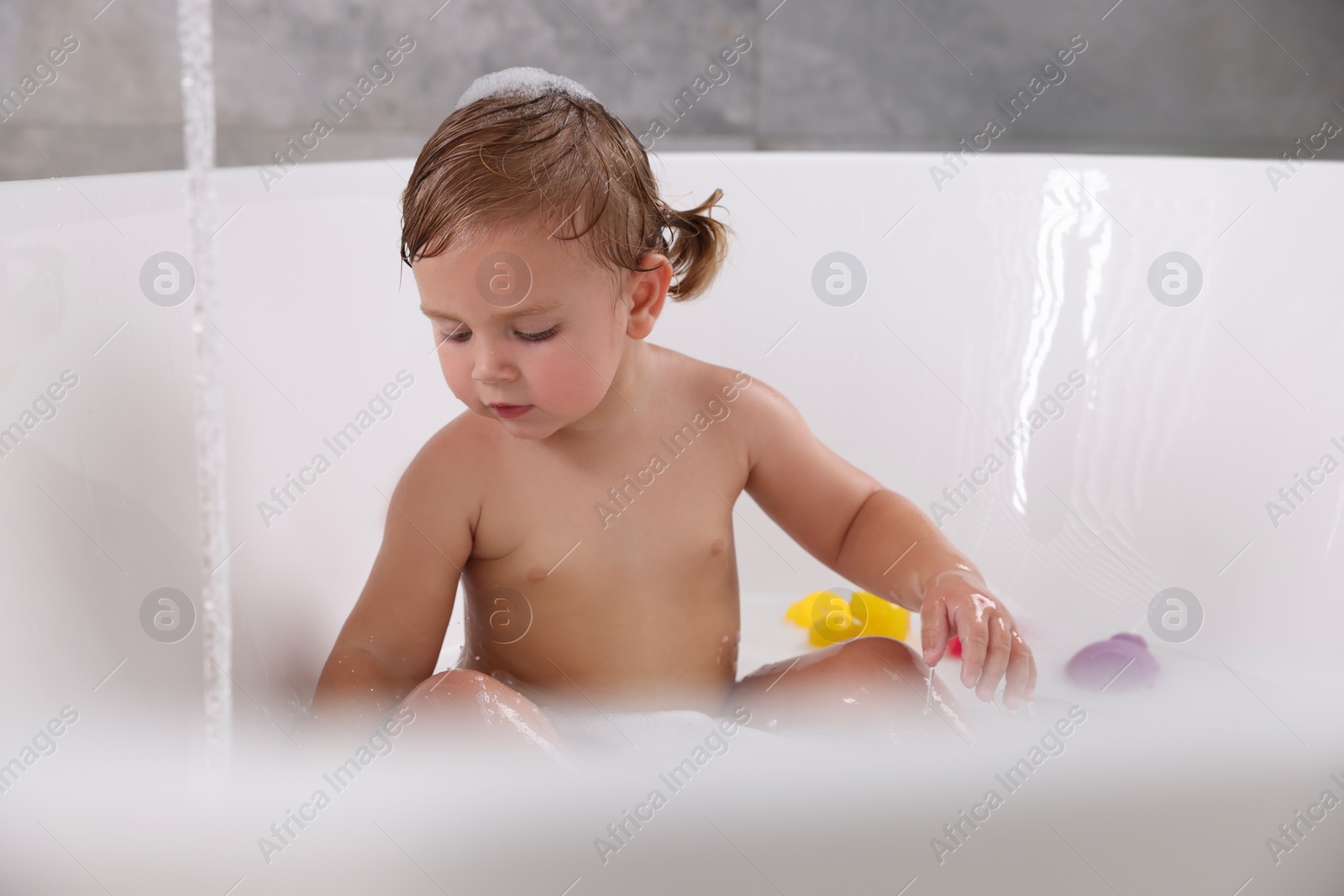 Photo of Cute little girl taking bubble bath with toys indoors