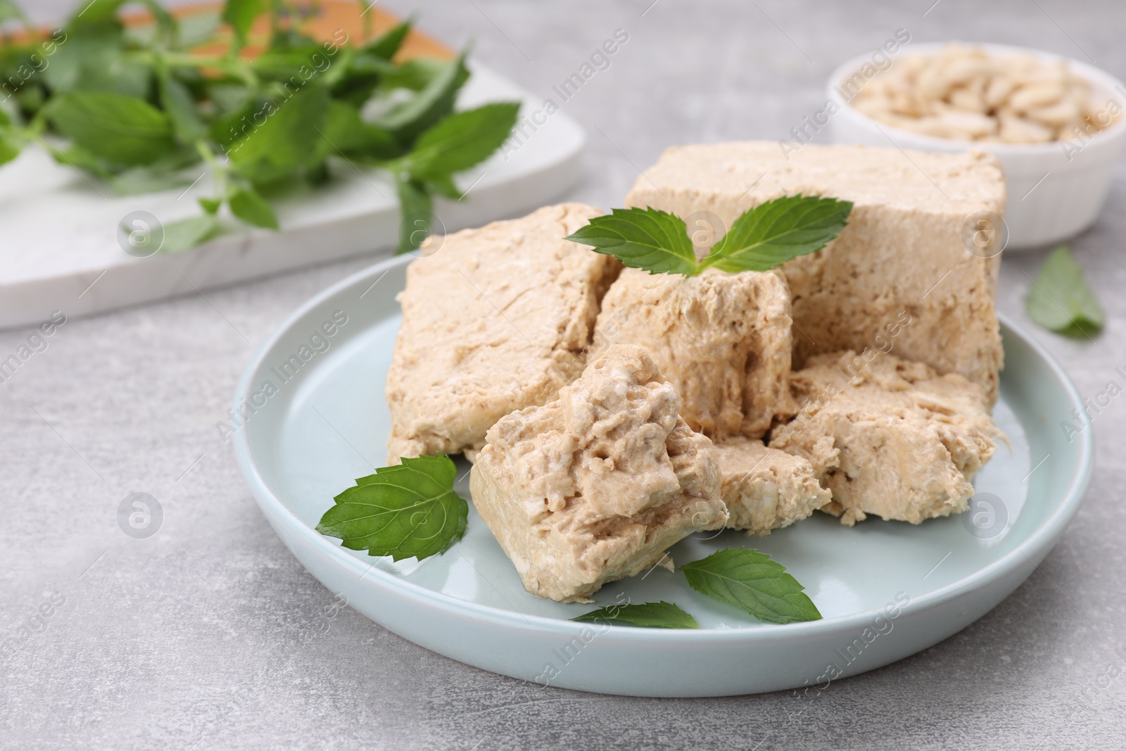 Photo of Plate with pieces of tasty halva and mint leaves on light grey table, closeup