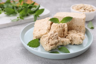 Photo of Plate with pieces of tasty halva and mint leaves on light grey table, closeup