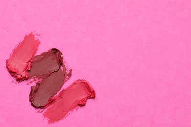 Photo of Smears of bright lipsticks on pink background, top view. Space for text