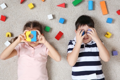 Cute children playing with colorful blocks on floor indoors, top view