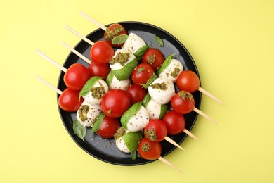 Caprese skewers with tomatoes, mozzarella balls, basil and pesto sauce on yellow background, top view