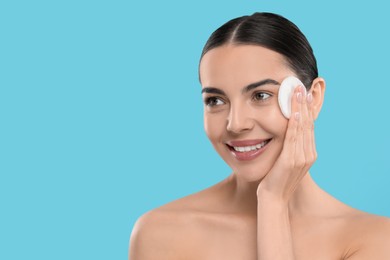 Photo of Beautiful woman removing makeup with cotton pad on light blue background, space for text