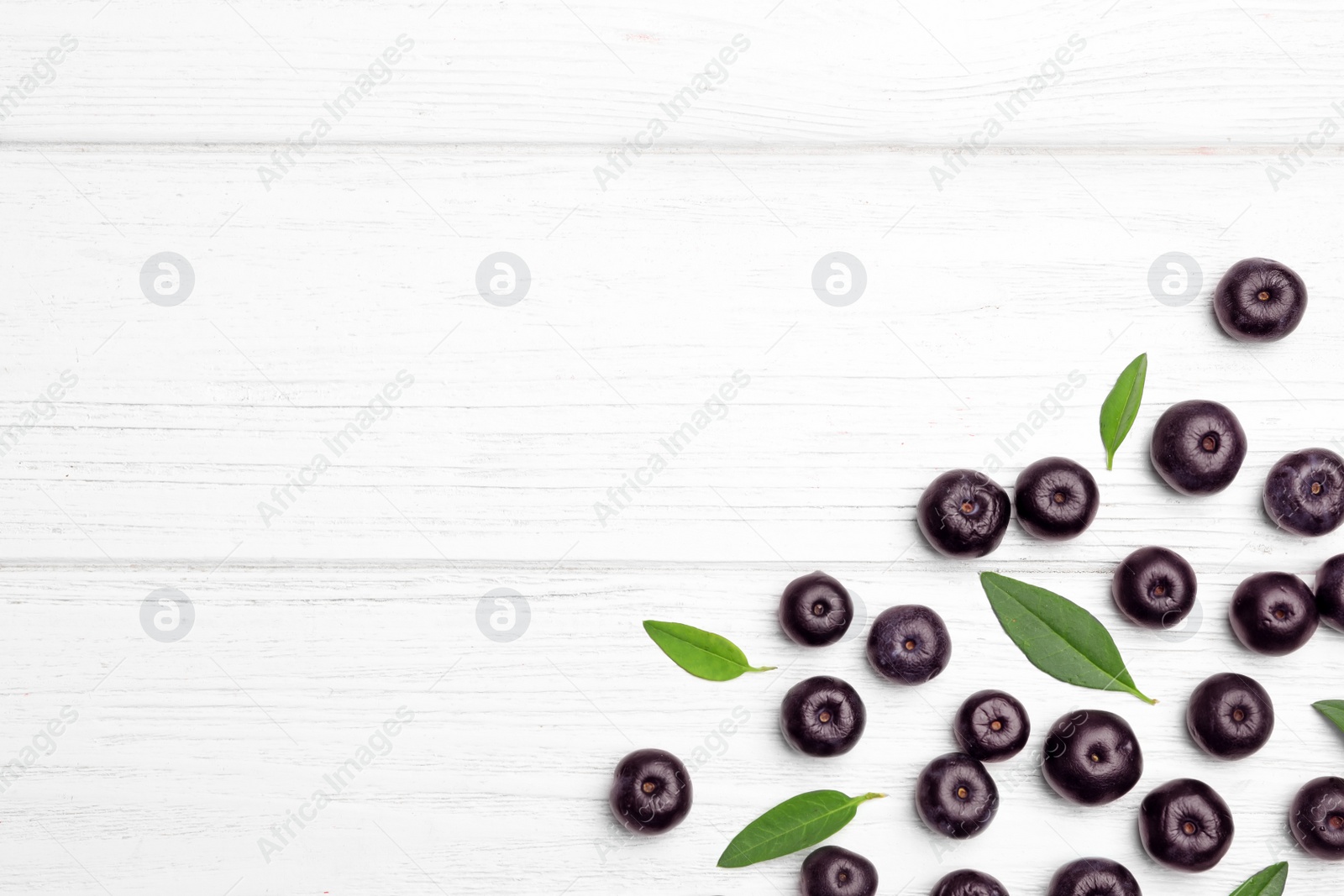 Photo of Fresh acai berries with leaves on white wooden table, flat lay. Space for text