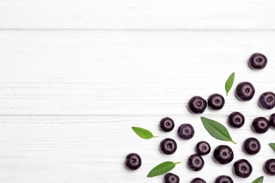 Photo of Fresh acai berries with leaves on white wooden table, flat lay. Space for text