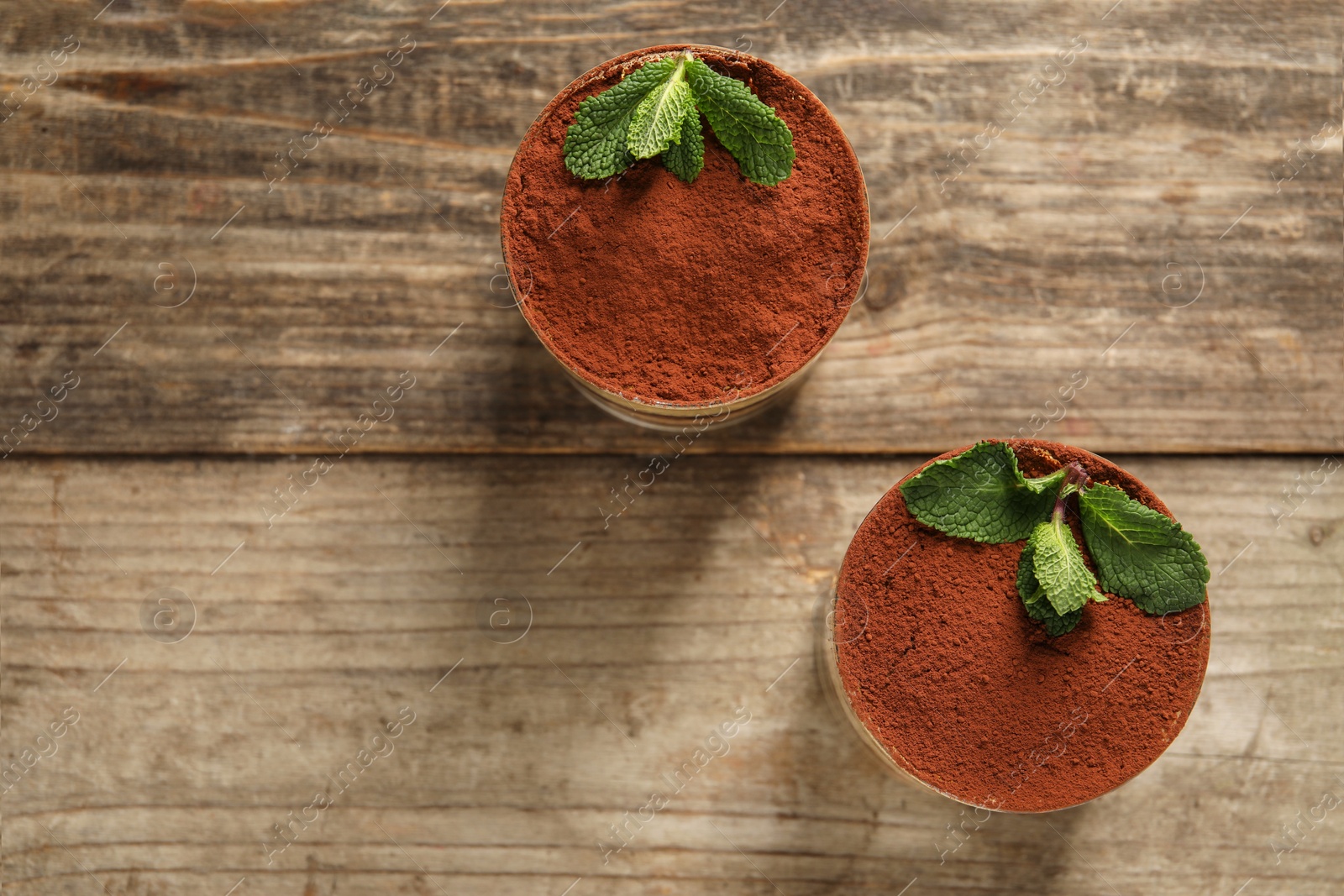 Photo of Tasty tiramisu and mint in glasses on wooden table, top view. Space for text