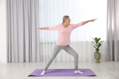 Senior woman practicing yoga on mat at home