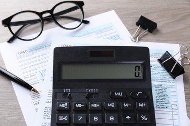 Photo of Tax accounting. Calculator, documents, glasses and stationery on wooden table, closeup