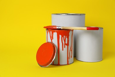 Photo of Cans of orange paint and brush on yellow background. Space for text