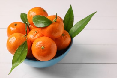 Photo of Fresh ripe juicy tangerines and green leaves in bowl on white wooden table, closeup. Space for text