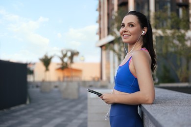 Beautiful woman in stylish sportswear listening music on city street, space for text