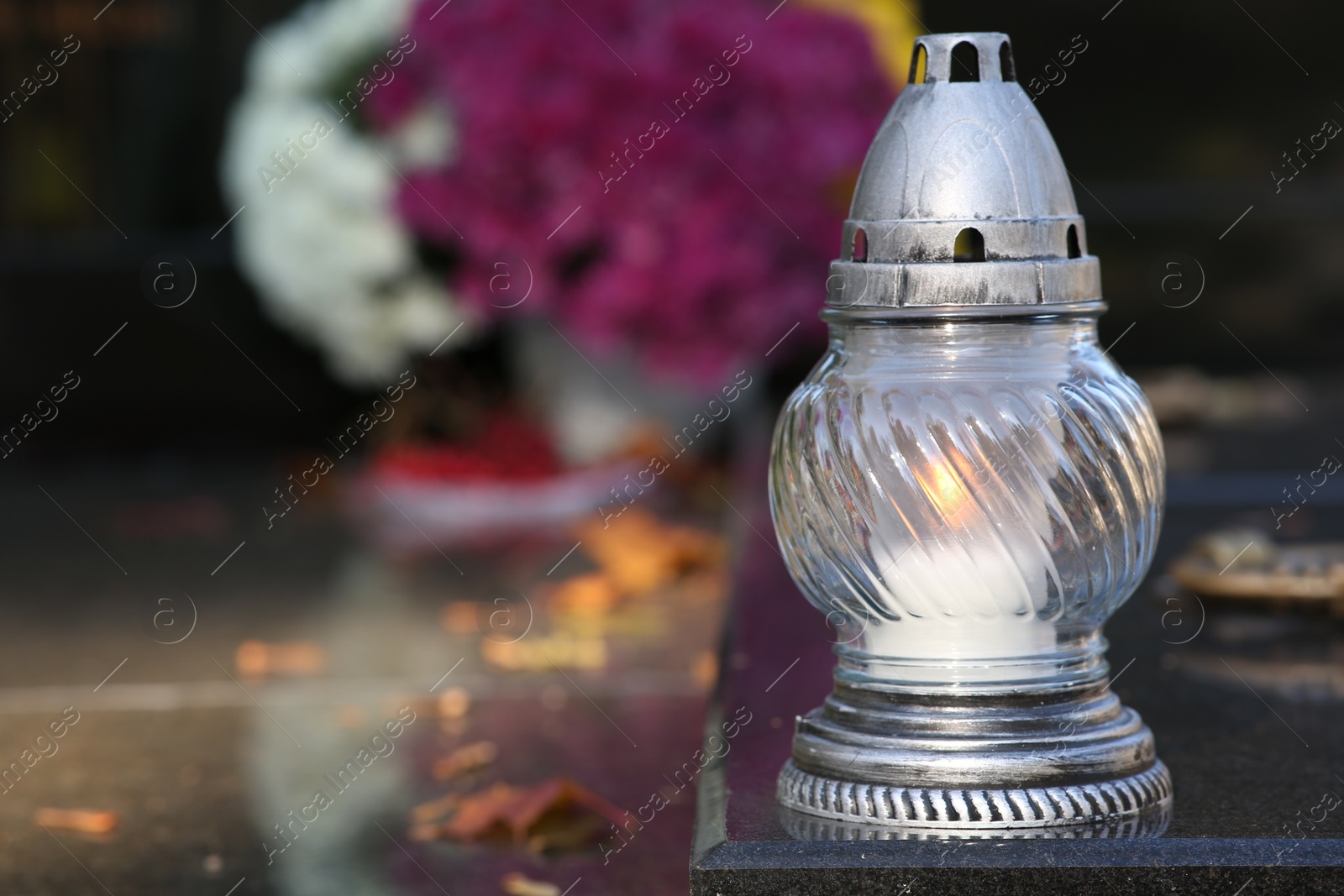 Photo of Grave lantern with burning candle on granite surface in cemetery, space for text