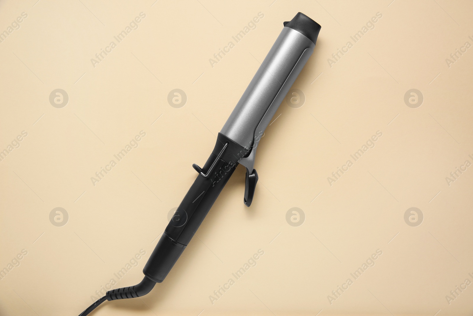 Photo of Hair curling iron on beige background, top view