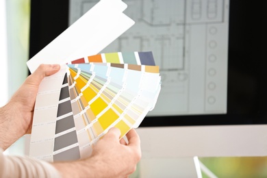 Designer with paint color palette samples at workplace, closeup