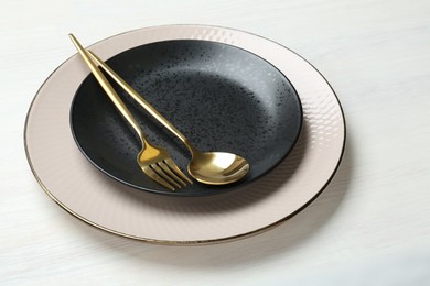 Stylish ceramic plates, fork and spoon on white wooden table, closeup
