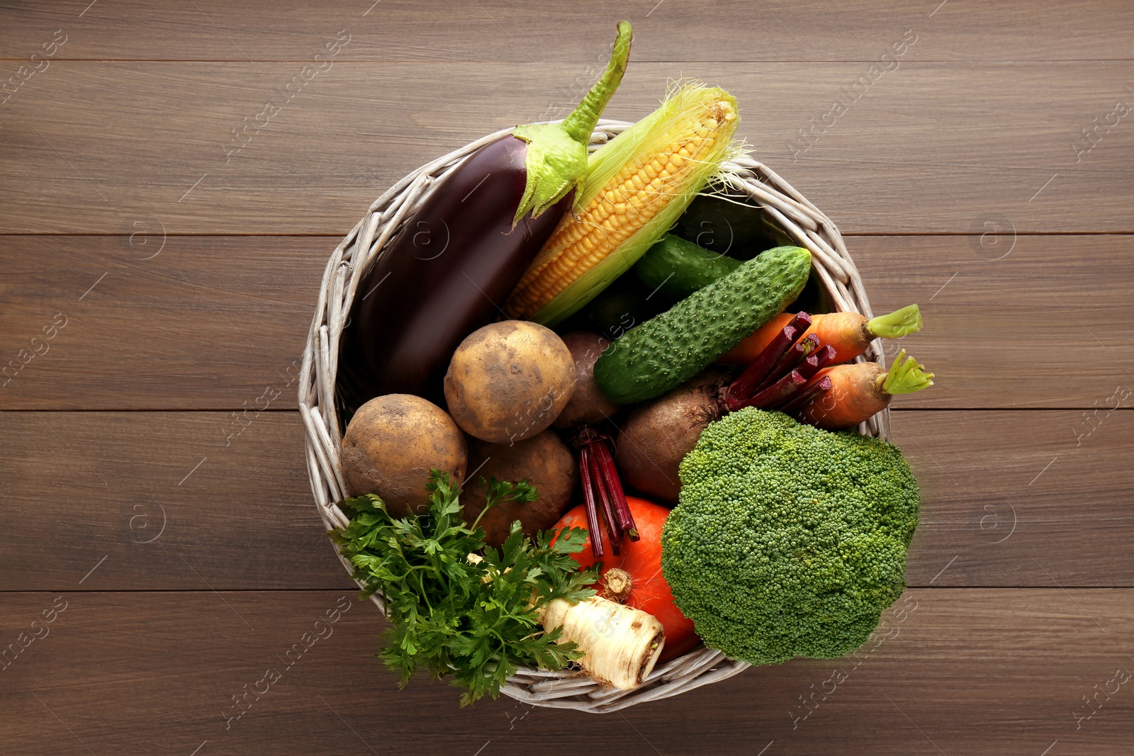 Photo of Basket with different fresh ripe vegetables on wooden table, top view. Farmer produce