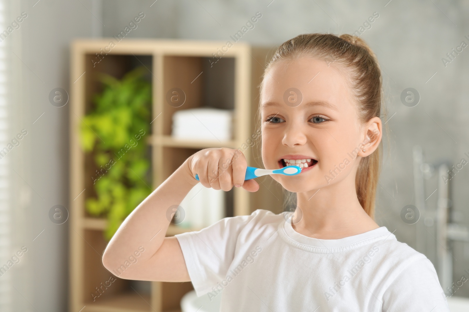 Photo of Cute little girl brushing her teeth with plastic toothbrush in bathroom, space for text