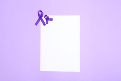 Purple awareness ribbons and blank card on lilac background, top view with space for text