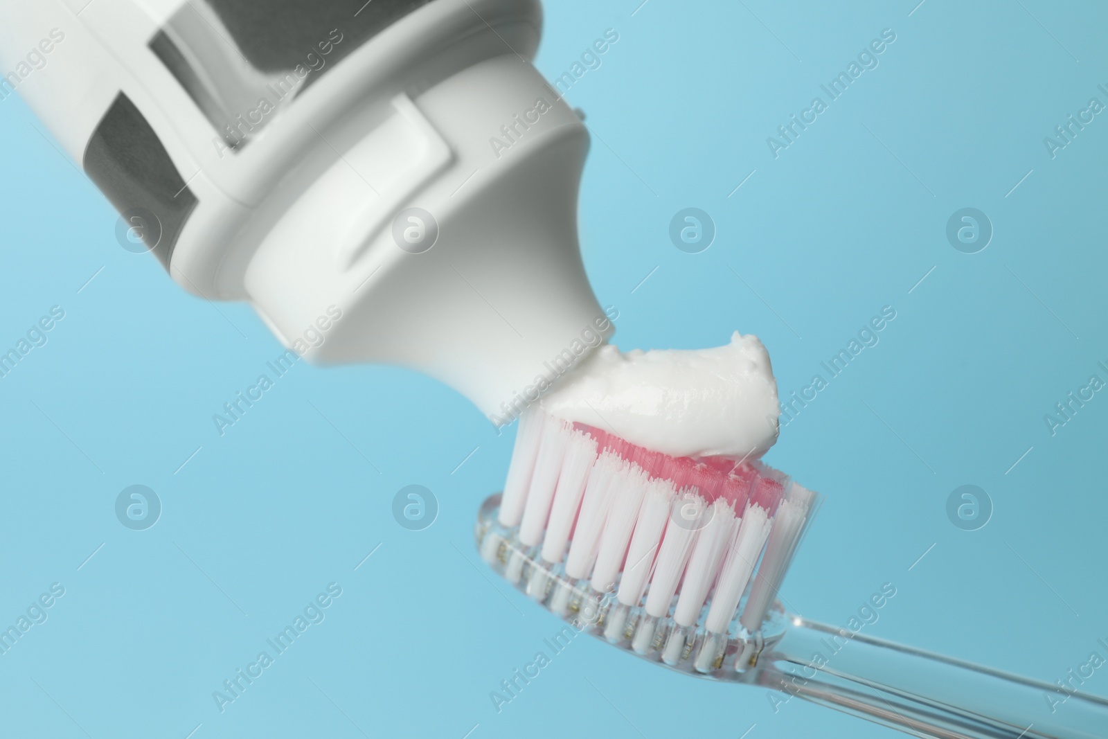 Photo of Squeezing toothpaste onto brush against turquoise background