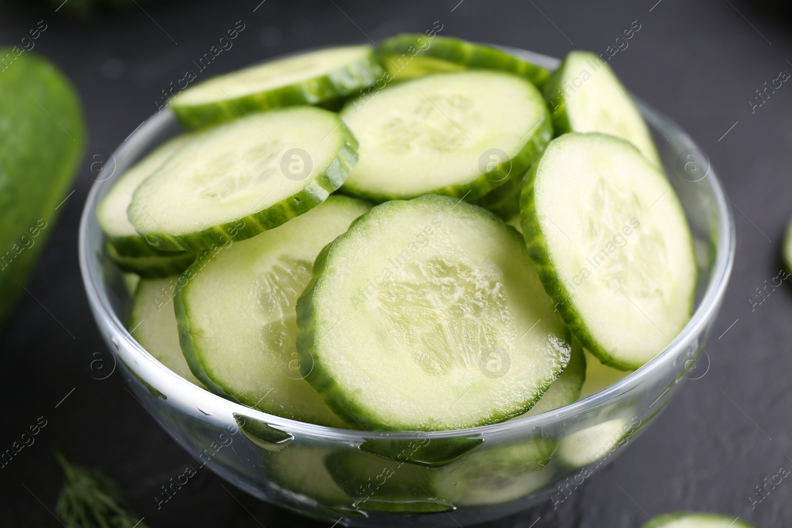 Photo of Cut cucumber in glass bowl on dark gray table, closeup