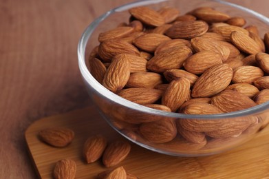 Bowl of delicious almonds on wooden table, closeup