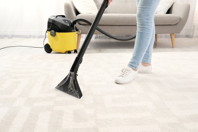 Photo of Woman removing dirt from carpet with vacuum cleaner indoors, closeup